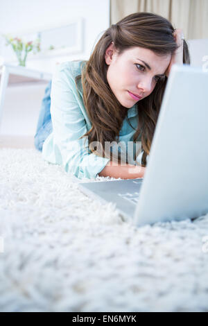 Focused woman using her laptop lying on the floor Stock Photo