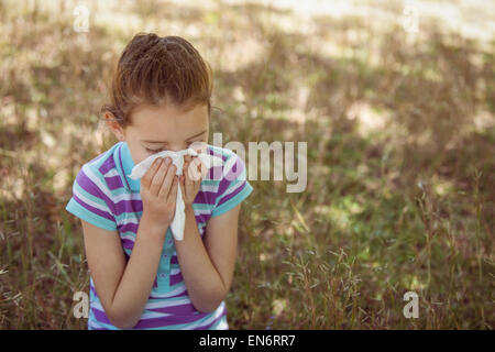 Cute little girl blowing her nose in park Stock Photo