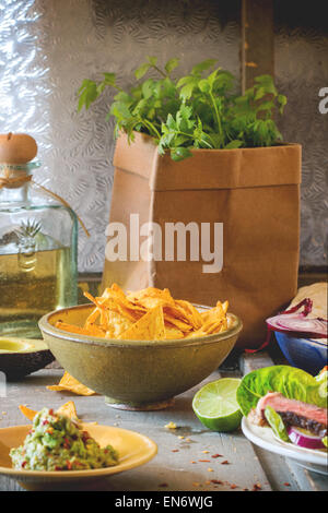Mexican style dinner with tacos, vegetables, nachos chips and guakomole, served over gray wooden table. Stock Photo