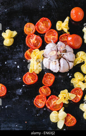 Pasta sacchettini and sun-dryed cherry tomatoes with garlic and sea salt over black metal oven-tray. Top view Stock Photo
