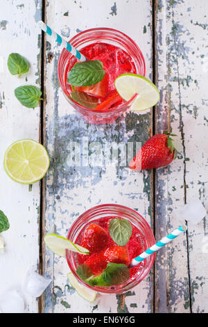 Two glasses with retro cocktail tubes and glass jug of homemade strawberry lemonade, served with fresh strawberries, mint, lime  Stock Photo