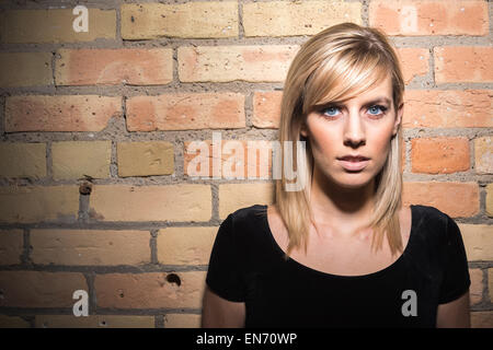 Portrait of attractive young blond woman in high contrast portrait against brick wall in skirt and black top with belly showing Stock Photo