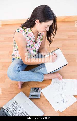 Pretty brunette writing on a paper while calculating Stock Photo