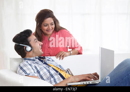 Young man listening to music while mother looks at laptop Stock Photo