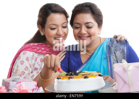 Woman cutting birthday cake while daughter looks on Stock Photo