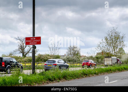 A 'New Road Layout Ahead' sign on a main road near a busy junction on the outskirts of Cirencester with moving traffic beyond Stock Photo