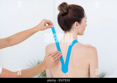 Physiotherapist applying blue kinesio tape to patients back Stock Photo
