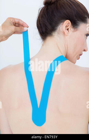 Physiotherapist applying blue kinesio tape to patients back Stock Photo