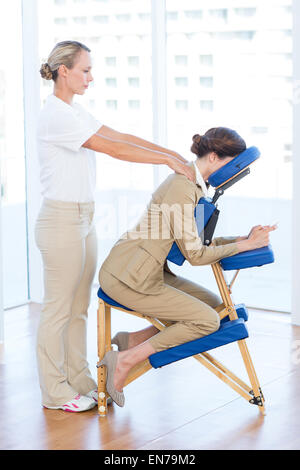 Businesswoman having back massage while using her mobile phone Stock Photo