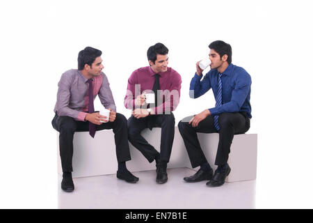 Male executive drinking tea as colleagues watch on Stock Photo