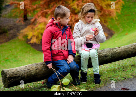 Boy and girl sitting together on the log in the autumn park Stock Photo