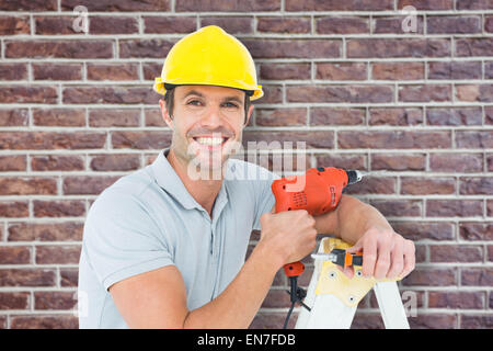 Composite image of happy technician holding drill machine while leaning on ladder Stock Photo