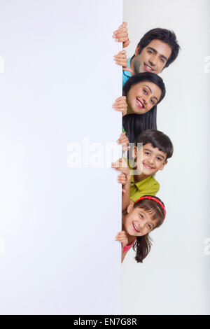 Portrait of family peeking behind white board Stock Photo