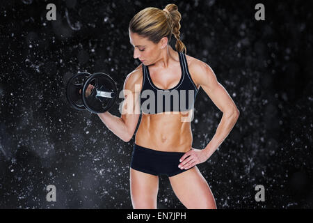 Composite image of female bodybuilder holding large black dumbbell with arm up looking at bicep Stock Photo