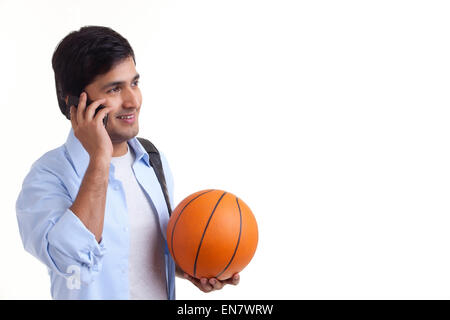 Portrait of smiling young man talking on mobile phone with basket ball
