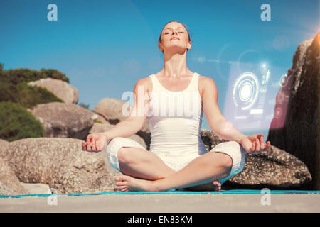 Composite image of blonde woman sitting in lotus pose on beach on mat Stock Photo