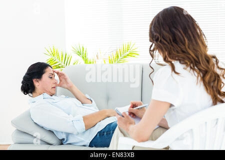 Depressed woman lying on the couch while her therapist taking notes Stock Photo