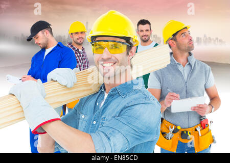 Composite image of carpenter wearing hardhat and glasses while carrying wooden planks Stock Photo