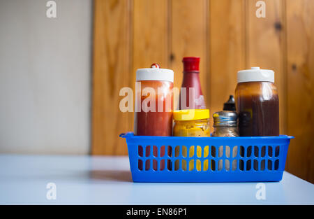 A cage in a cafe containing salt, pepper and various sauces including mustard, brown sauce, vinegar and ketchup. Stock Photo