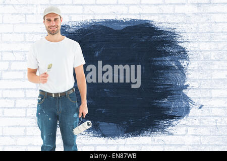 Composite image of happy man holding paint roller and paintbrush Stock Photo