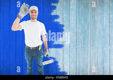 Composite image of happy man wearing gloves while holding paint roller Stock Photo