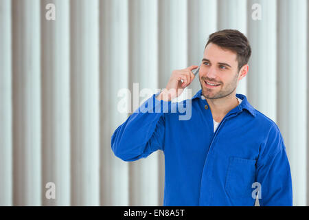 Composite image of happy young male mechanic using mobile phone Stock Photo