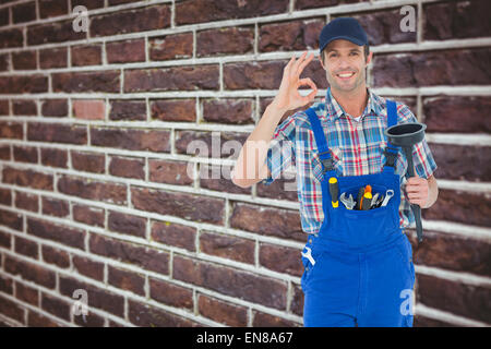 Composite image of plumber holding plunger while gesturing ok sign Stock Photo