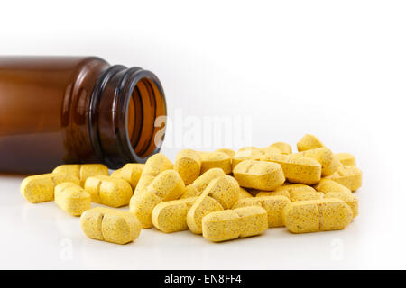 Yellow pills fallen out of brown bottle, is emptied. Studio shot on white background. Stock Photo