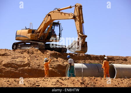 Excavator assisting workers laying concrete pipes on a construction site Stock Photo