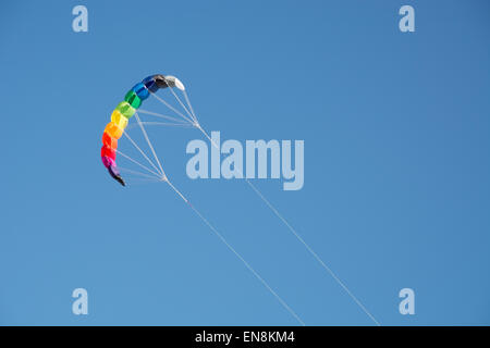 Colourful stripped kite flying high in the blue sky with visible strings and cords Stock Photo