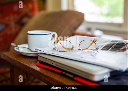 Still life study of cup and saucer, reading glasses, magazine and laptop Stock Photo