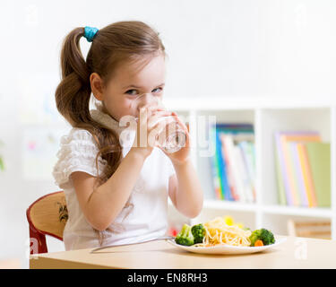 Cute little girl drinking water sitting at table in nursery Stock Photo