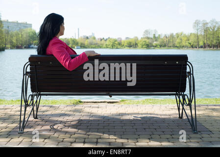 Solitude- Sad woman sitting on bench in park looking to the water Stock Photo