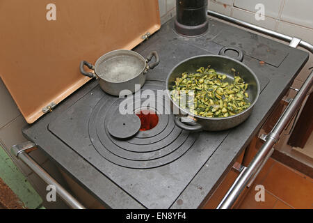 pan with zucchini baked in cast iron stove with fire lit in the old mountain home Stock Photo