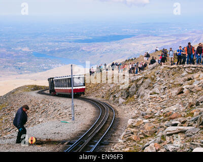 Snowdon railway train leaving summit for Llanberis busy with people walking up on a trackside path in Snowdonia National Park North Wales UK Britain Stock Photo