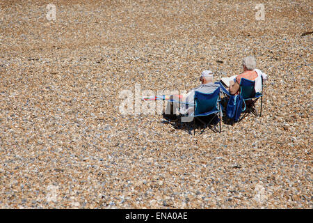 Elderly couple relaxing in chairs on a shingle beach look out to sea Stock Photo