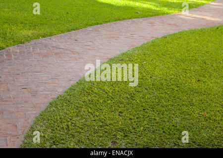 Curved red brick walkway with green grass around it Stock Photo