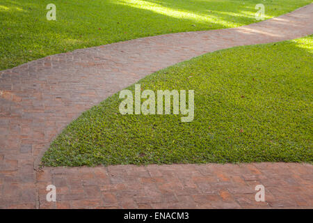 Curved red brick walkway with green grass around it Stock Photo