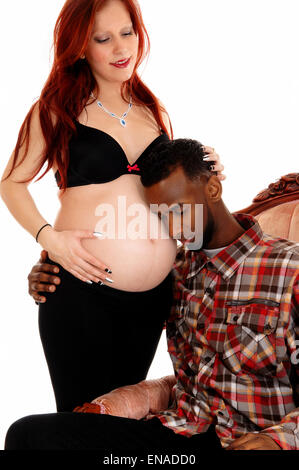 An African American man holding his ear on his wife's baby belly, isolated for white background. Stock Photo