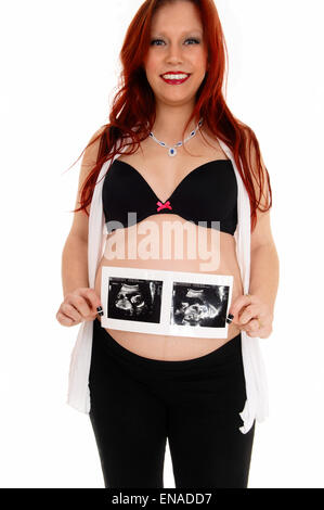 A happy young pregnant woman holding the ultrasound picture for her belly, isolated for white background. Stock Photo