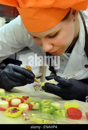 Oldisleben, Germany. 10th Apr, 2015. Master confectionist, Juliane Siedler, works on pralines in the display area of Karin Finger's Goethe Chocolate Factory in Oldisleben, Germany, 10 April 2015. The colorful high-heeled shoes are part of the extensive, high-quality praline production at her company, which was founded ten years ago. Photo: WALTRAUD GRUBITZSCH/dpa/Alamy Live News Stock Photo