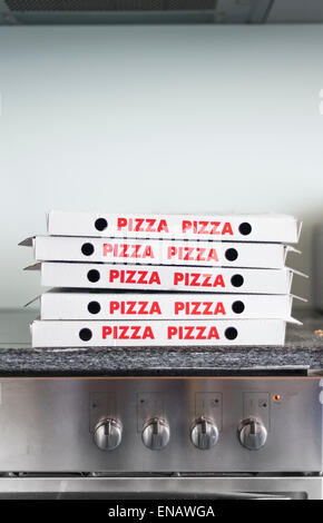 A pile of many Pizza cardboard boxes is stacked on top of a stove. Stock Photo