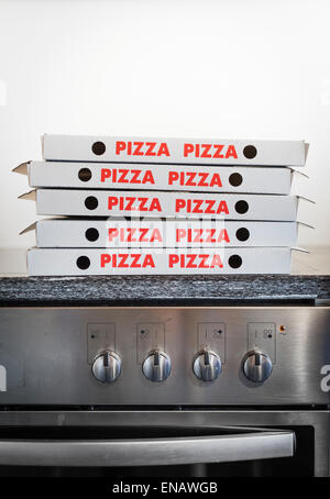 A pile of many Pizza cardboard boxes is stacked on top of a stove. Stock Photo
