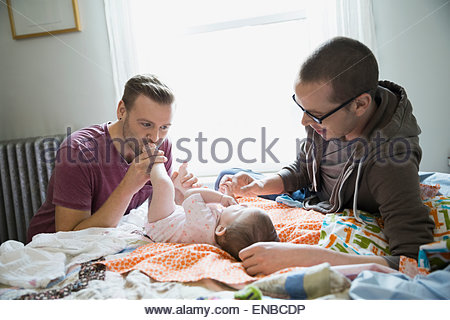 Homosexual couple playing with baby on bed