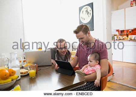 Homosexual couple using technology with baby daughter table
