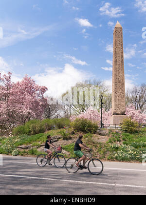 Springtime view of couple cycling past the Egyptian Obelisk in Central Park, NYC, USA Stock Photo