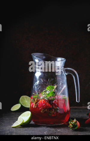 Glass jug of strawberry lemonade, served with fresh strawberries, mint and  lime over dark background. See series Stock Photo