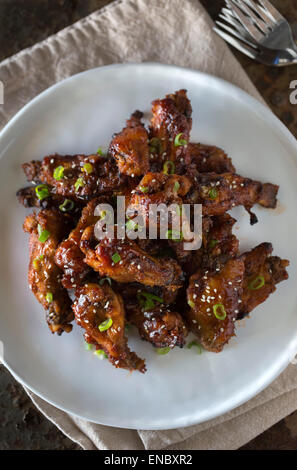 Asian-Style Sticky Chicken Wings sprinkled with sesame seeds and scallions served on a white plate. Stock Photo