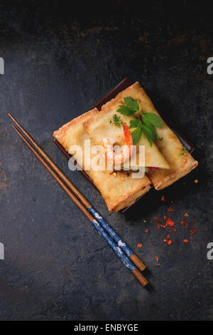 Fried spring rolls with vegetables and shrimps, served on squer ceramic plate with chopsticks over black background. Stock Photo