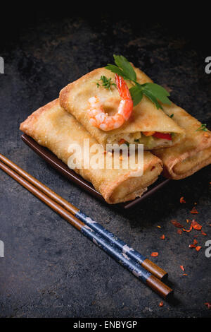 Fried spring rolls with vegetables and shrimps, served on squer ceramic plate with chopsticks over black background. Stock Photo